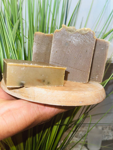 Noureture By Nature’s Neem Handmade Soap. Handmade Vegan Soap. Organic Ingredients Soap. All-Natural Handmade Soap. Cruelty Free Ingredients Soap. Small Business Soap. Black Women in Business Soap. Male Holding Soap on circular wooded board, in hand next to blue back drop. Nigerian Shea Butter Handmade Soap.